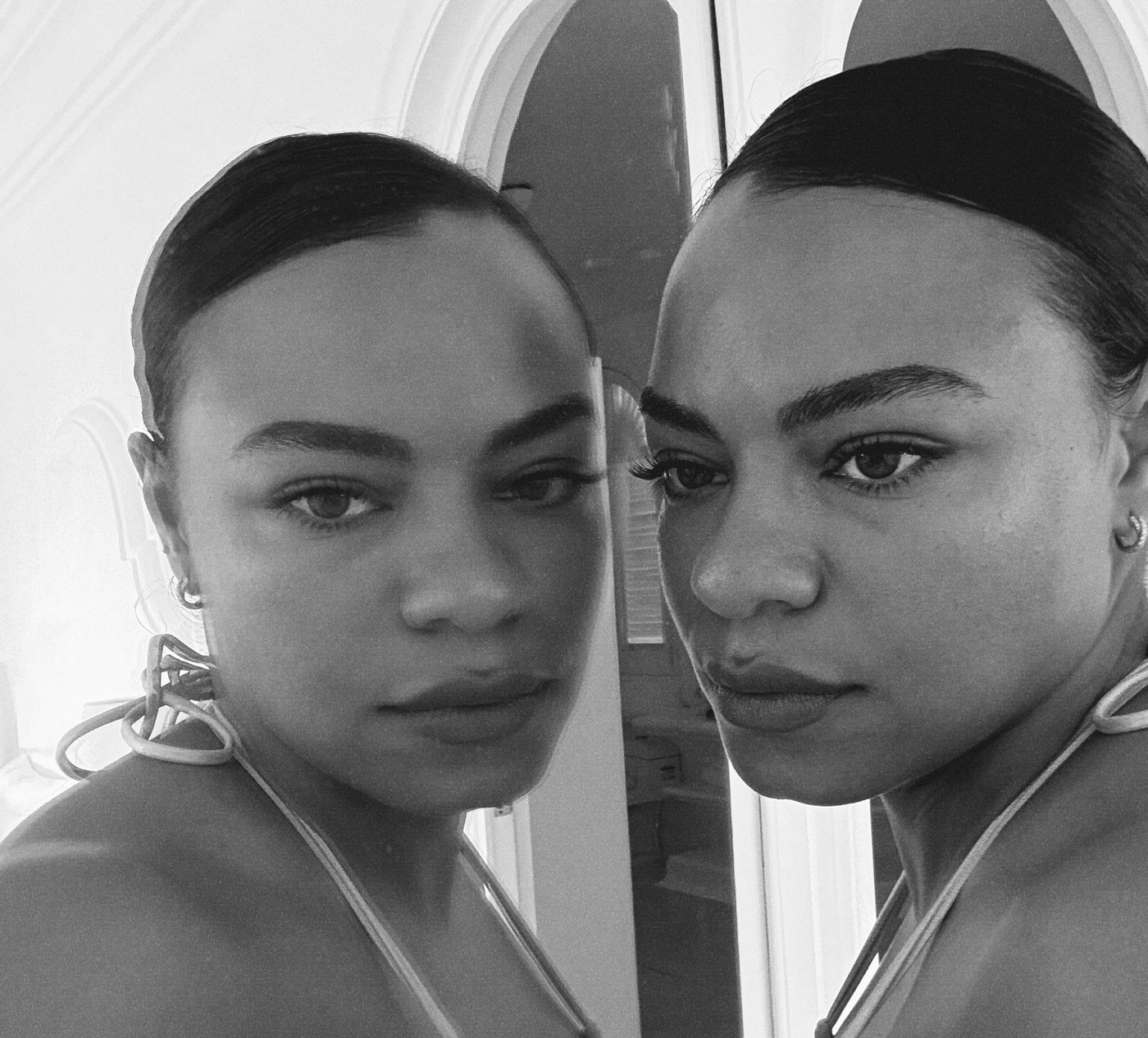 Black-and-white mirrored double portrait of Amanda, hair pulled back, looking into the camera.